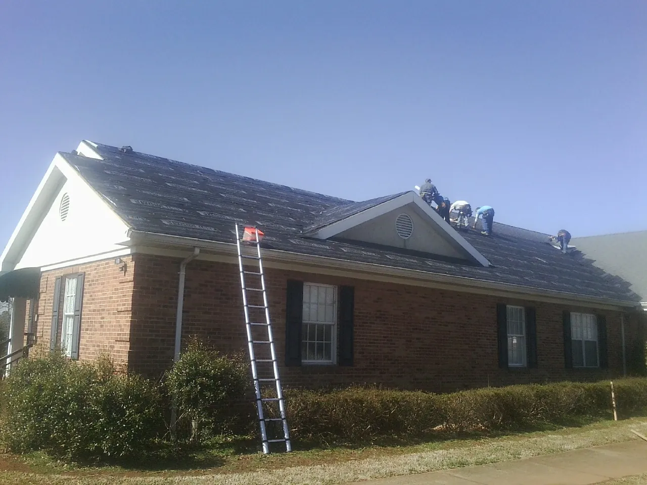 Crew tearing shingles off a brick ranch roof with a ladder set — Emergency Roof Repair work by our crew in Duchesne