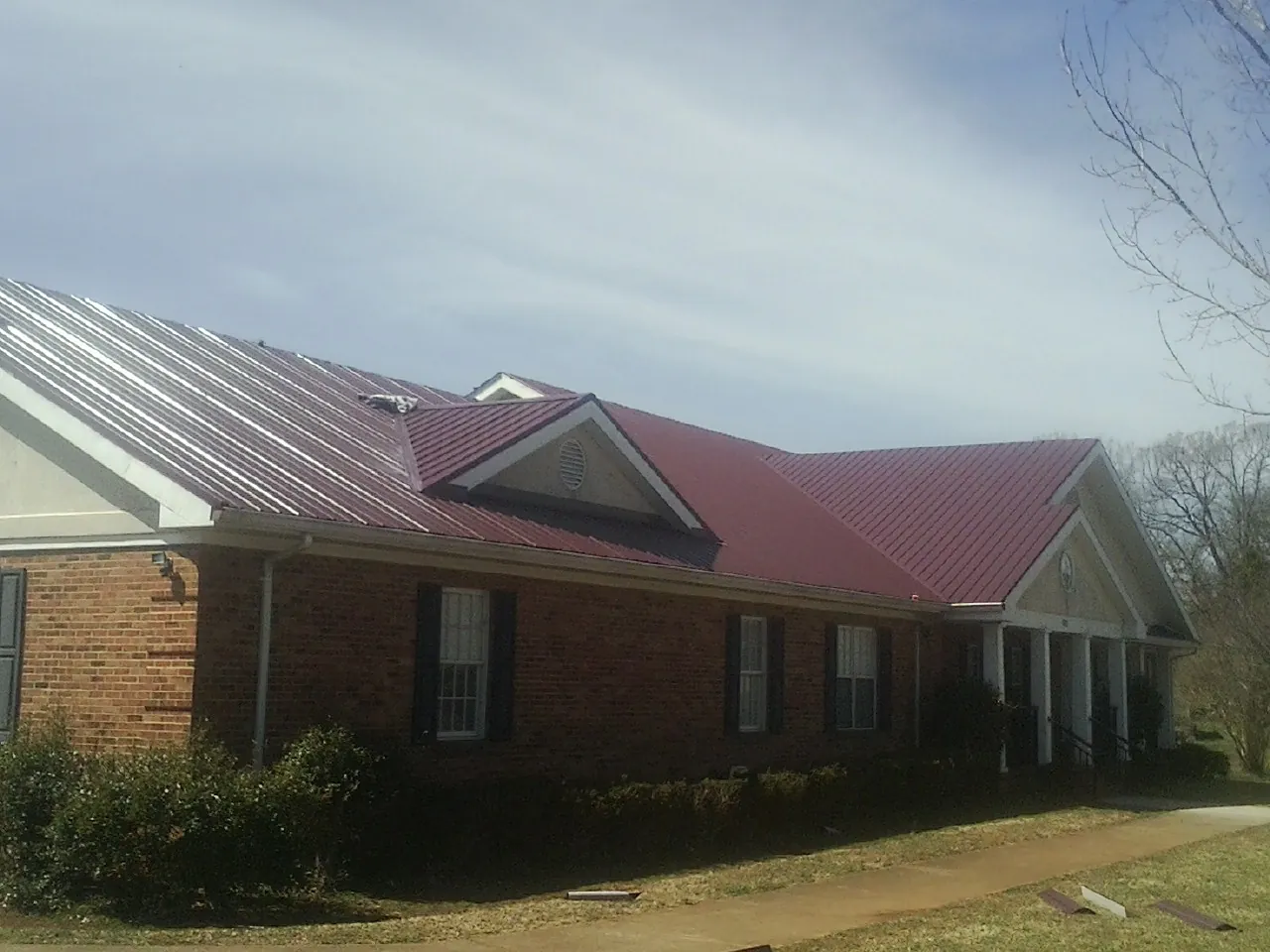 Red metal roof with gabled entries on a long brick building, from a Hail Damage Roof Repair job in Duchesne
