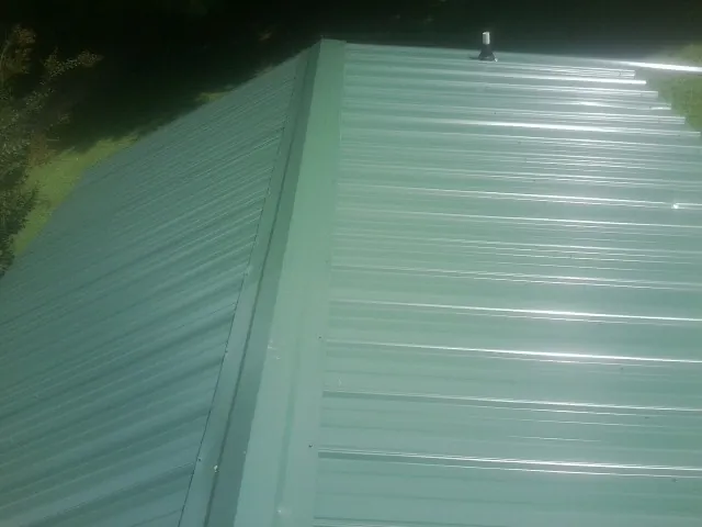 New green metal panels meeting at the ridge of a roof — Flat Roof Repair work by our crew in Duchesne
