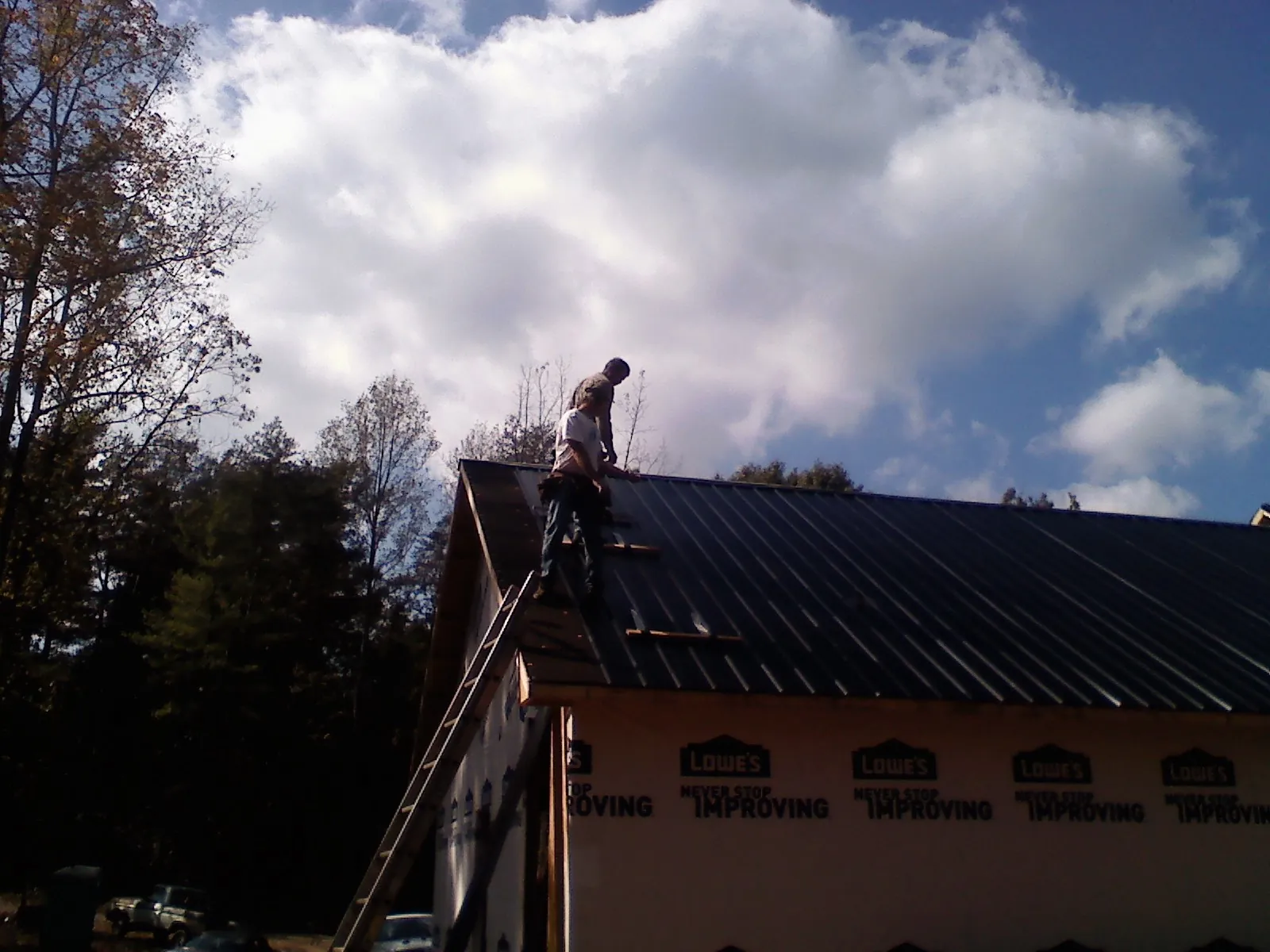 Roofer fastening dark metal panels high against a cloudy sky, from a Roof Inspection job in Duchesne