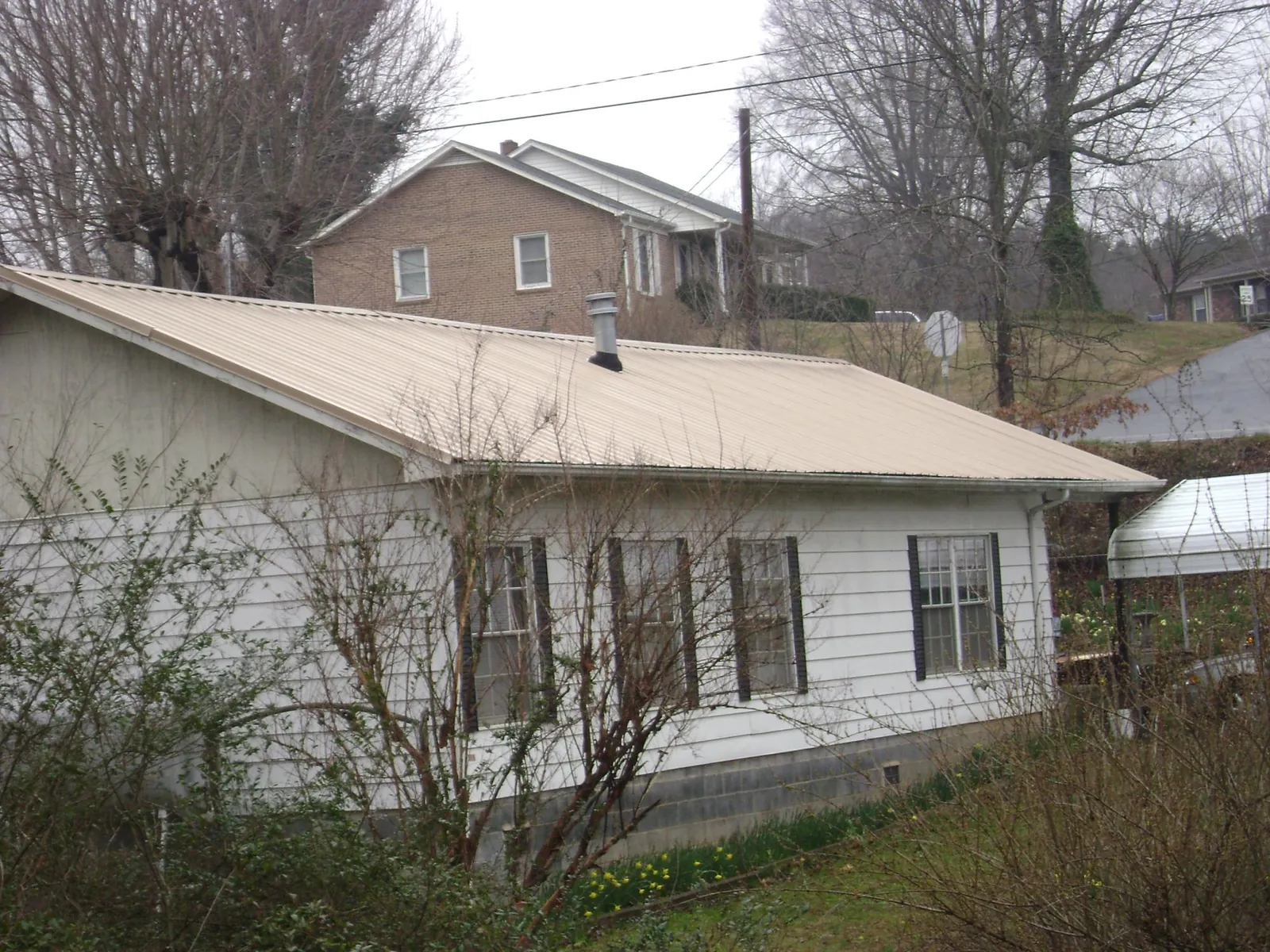 Tan metal roof on a white sided house set into a hillside — Commercial Roofing by Roofing Brothers in Duchesne