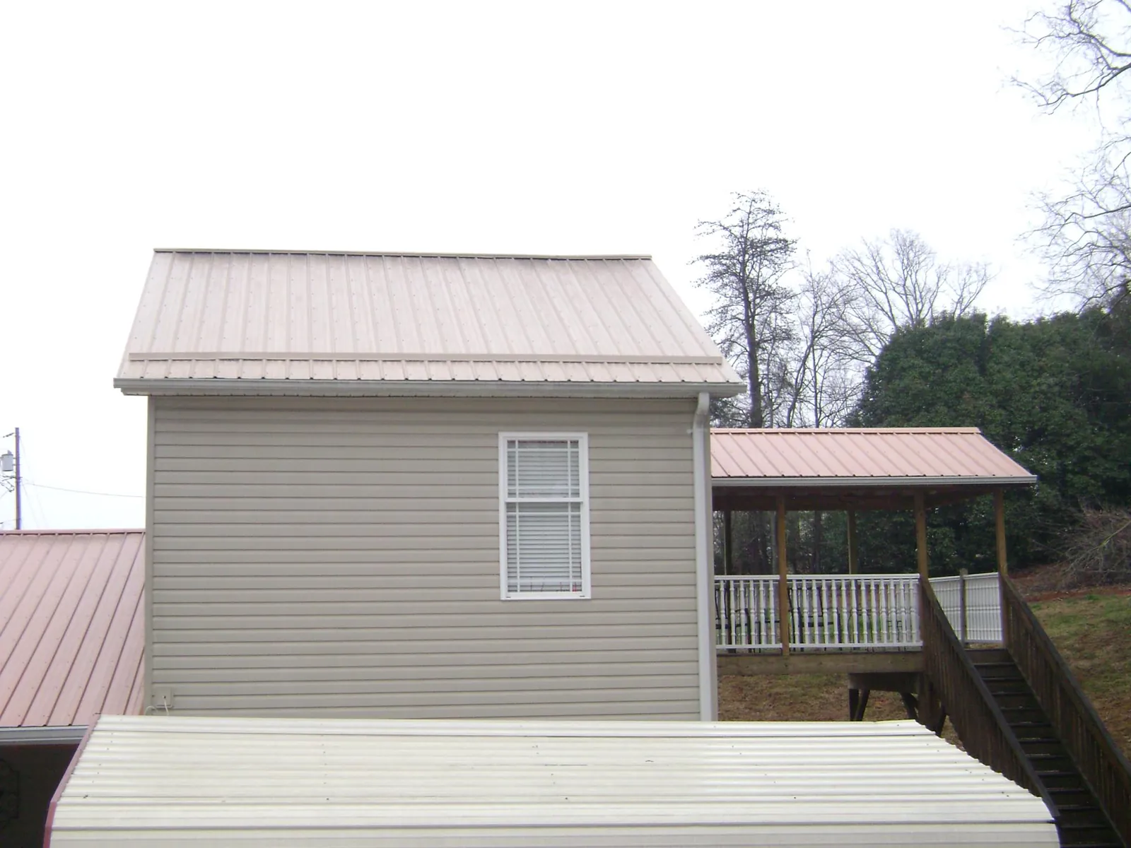 Tan metal roofs on a two story addition and attached porch, from a Roof Replacement job in Duchesne
